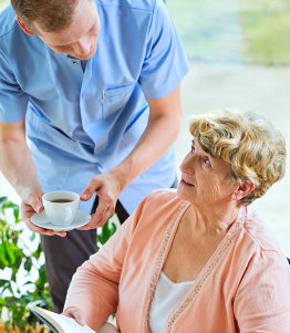 a nurse serving tea to his senior patient