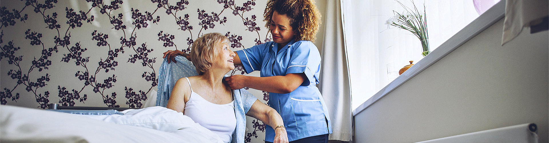 a woman helping her elderly patient dress up.